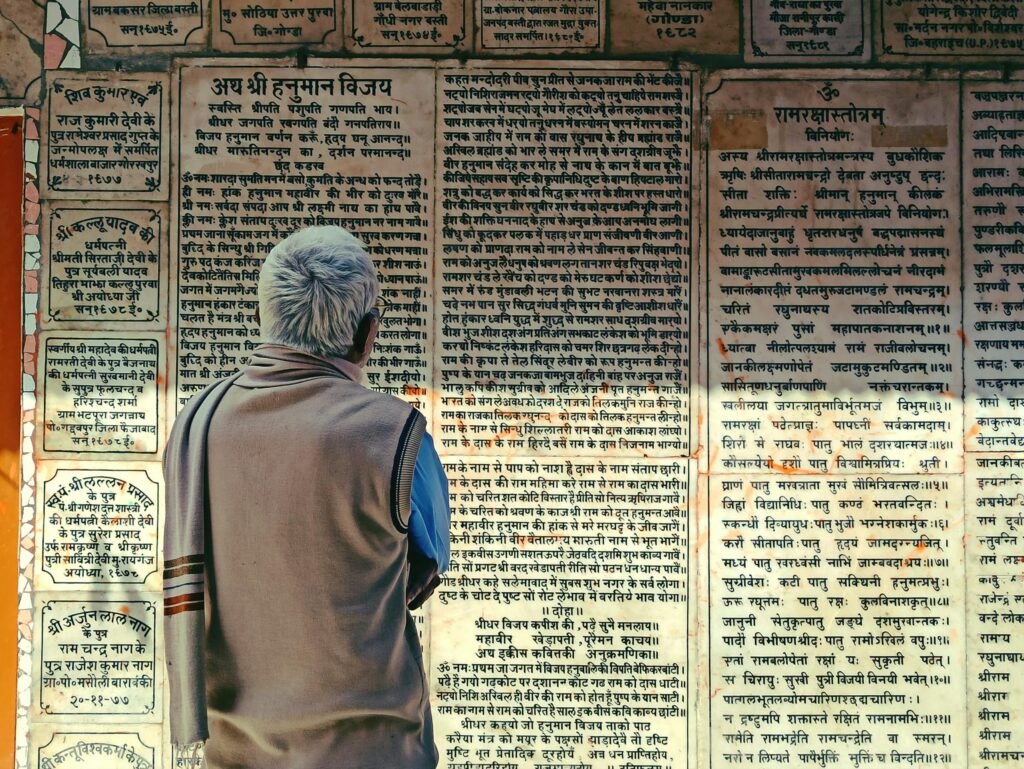 Elderly man reads ancient scriptures on temple wall in Bodh Gaya, India, rich in cultural heritage.