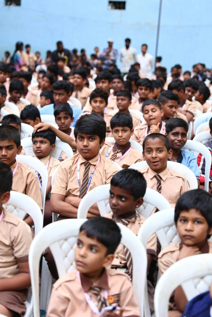 Indian school boys in uniform attending an outdoor school assembly event, seated in rows.